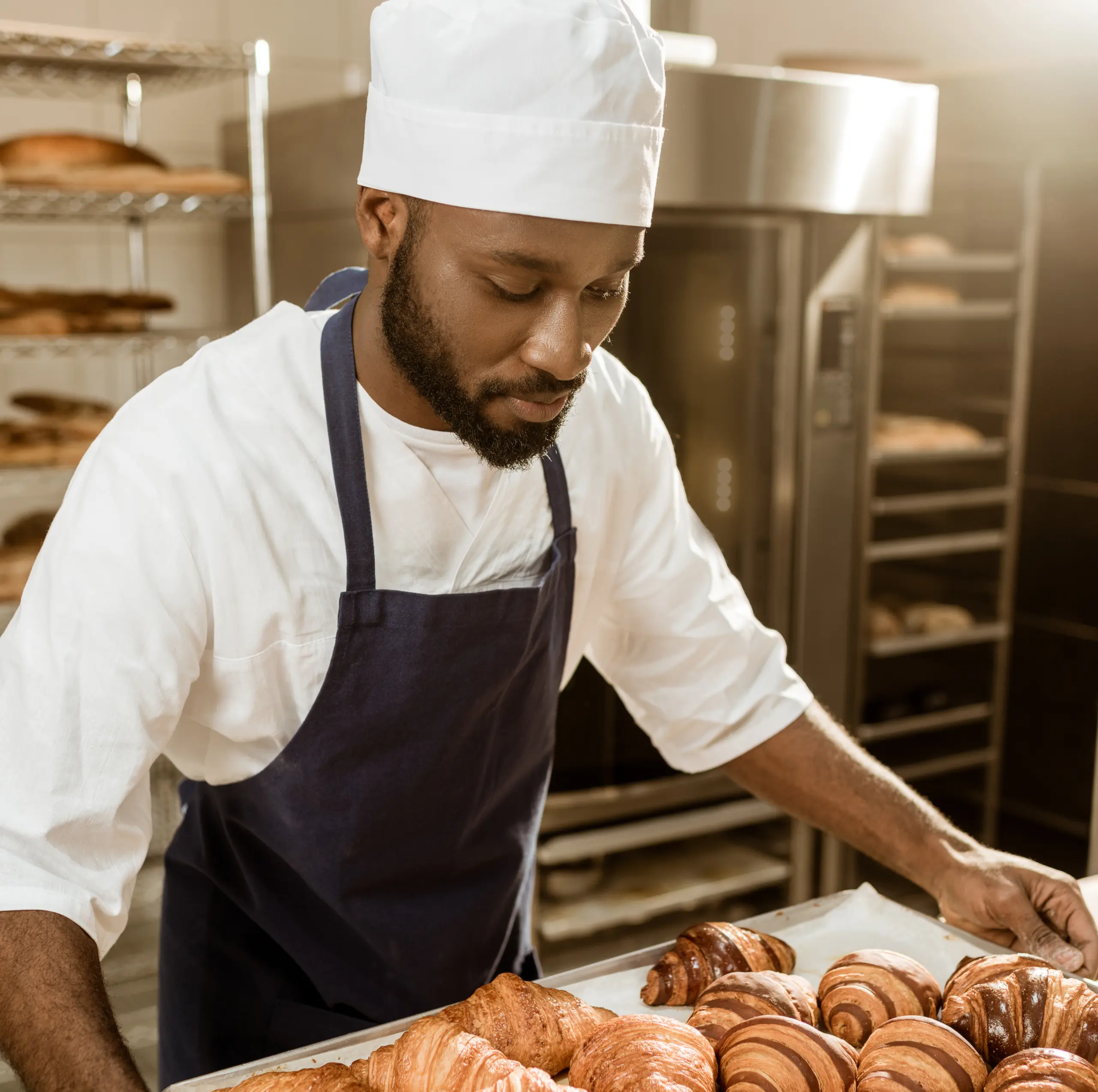 chef wearing apron and hat carrying baked goods